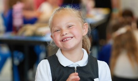 A child smiling broadly to camera in class