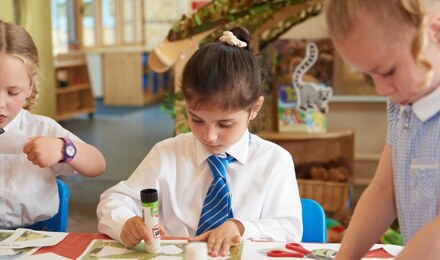Three children cutting and sticking in reception
