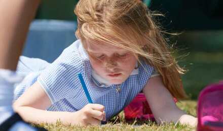 A child colouring whilst laying on grass