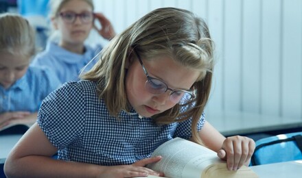 A child wearing glasses studies a reading book intently