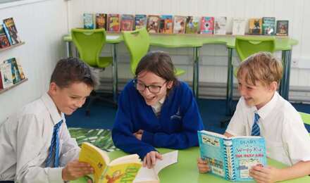 Three children laughing whilst sharing a book